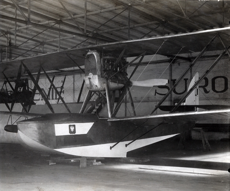 Łódź latająca typu Macchi M-9 w hangarze. Dobrze widoczny napis „Palenie Surowo”, a także schody w tylnej ścianie hangaru.